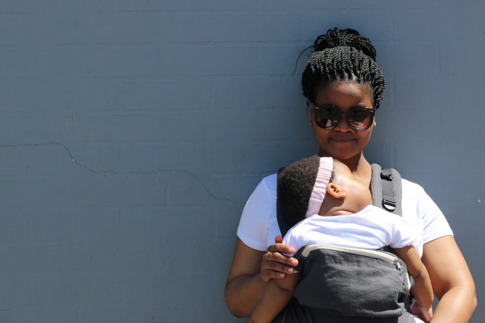 Woman holding a baby in carrier against a wall